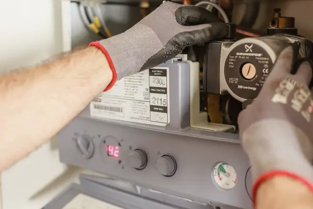 Technician's gloved hands testing the control board of a heating unit