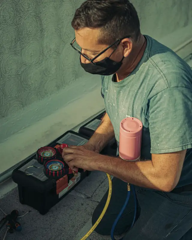 Technician kneeling beside an open toolcase, connecting gauges to a unit