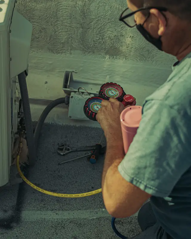 Technician in a green shirt servicing an outdoor unit with tools laid out