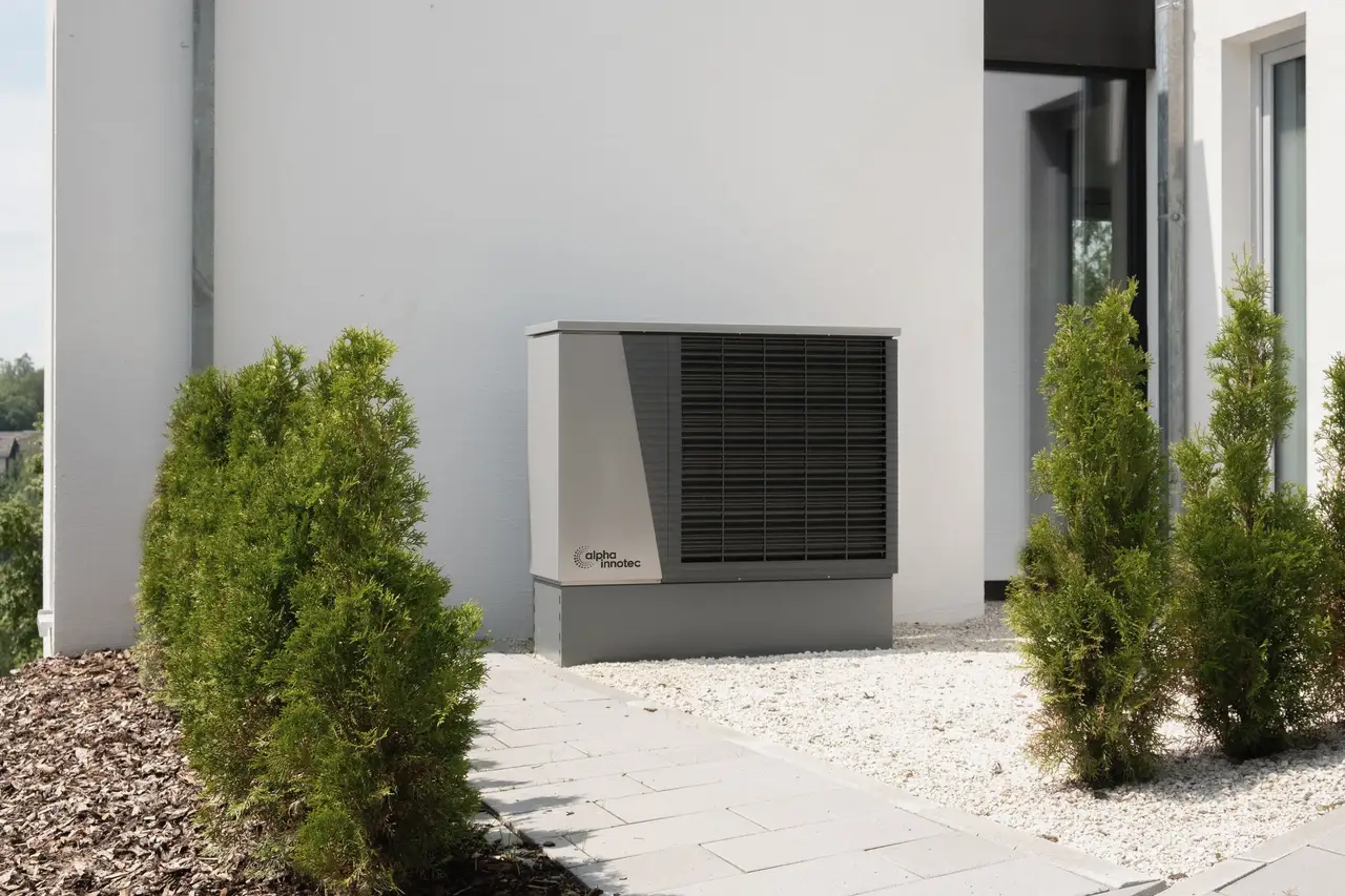 Outdoor heat pump unit set on a pad beside the white wall of a house